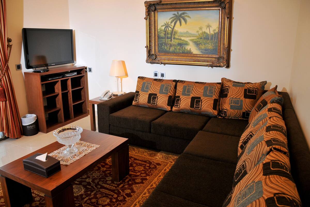 A living room with a sofa, a coffee table, a TV, and a painting on the wall.