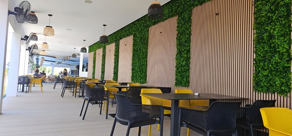 A restaurant with outdoor seating, yellow and black chairs, and green vertical gardens on the walls.