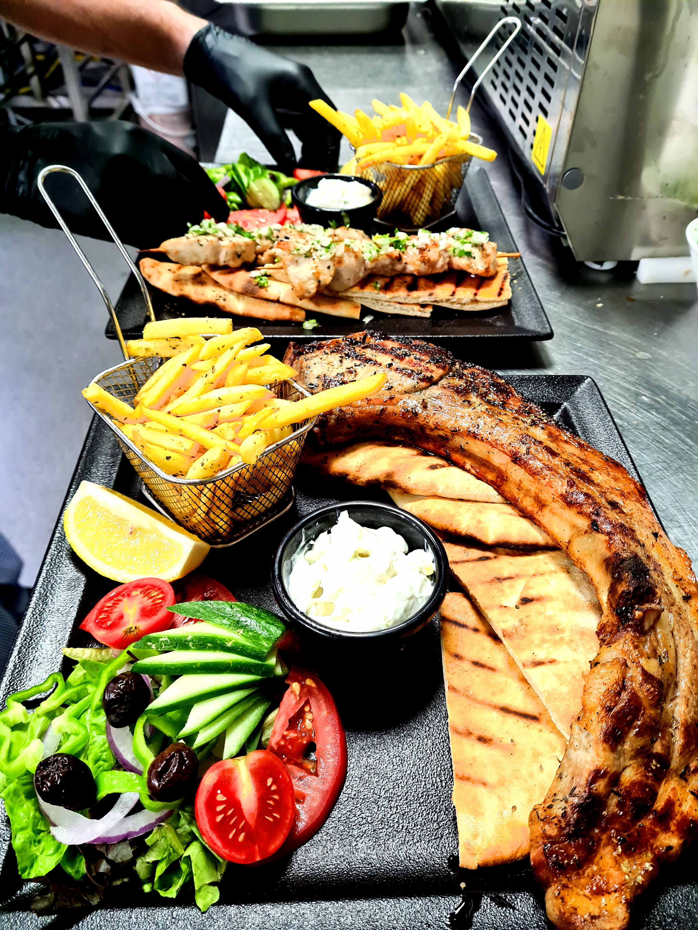 A tray of grilled fish, French fries, and a salad with a lemon wedge and two bowls of sauce.