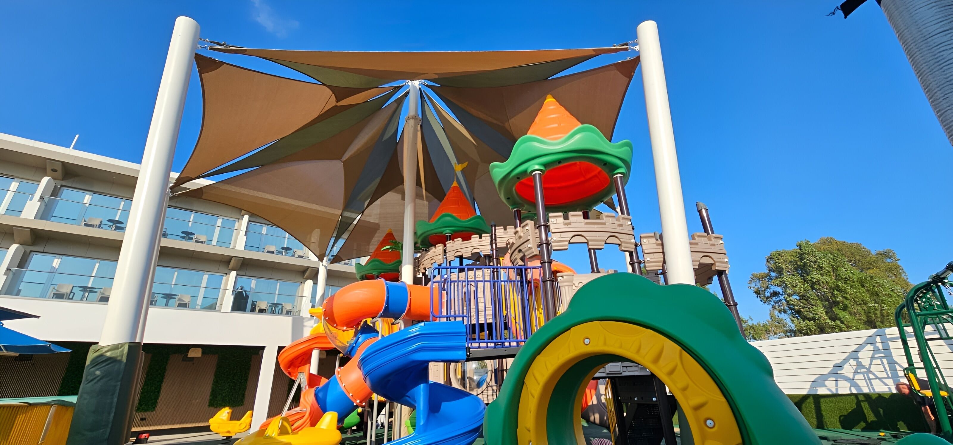 Un espace de jeux pour enfants avec un toboggan et des structures d’escalade, situé devant un bâtiment moderne doté de balcons.