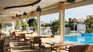 A poolside area with wooden furniture, a pool, and umbrellas. - Sveltos Hotel (Oroklini)