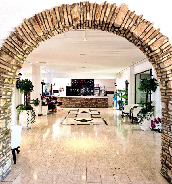 A lobby with a stone archway, a reception desk, and potted plants. - Sveltos Hotel (Oroklini)