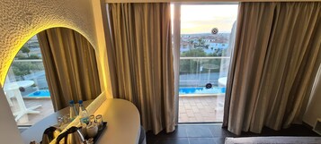 Una habitación con un ventanal grande, una mesa blanca con botellas y vasos, y vistas a una piscina y casas exteriores.