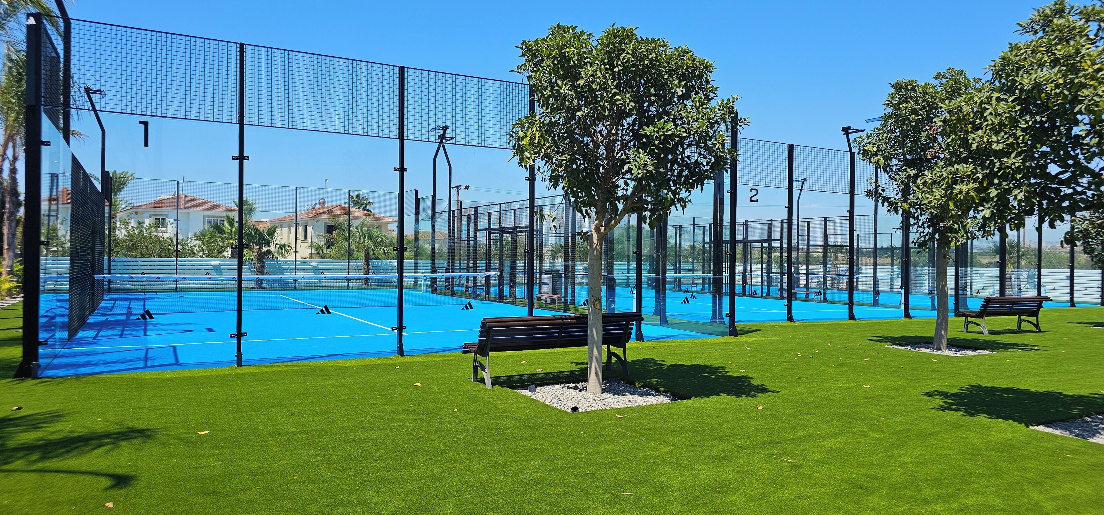 Un campo da tennis con una rete, circondato da una recinzione e panchine sull'erba.