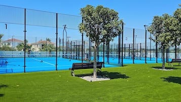 Un campo da tennis con una rete, circondato da una recinzione e panchine sull'erba.