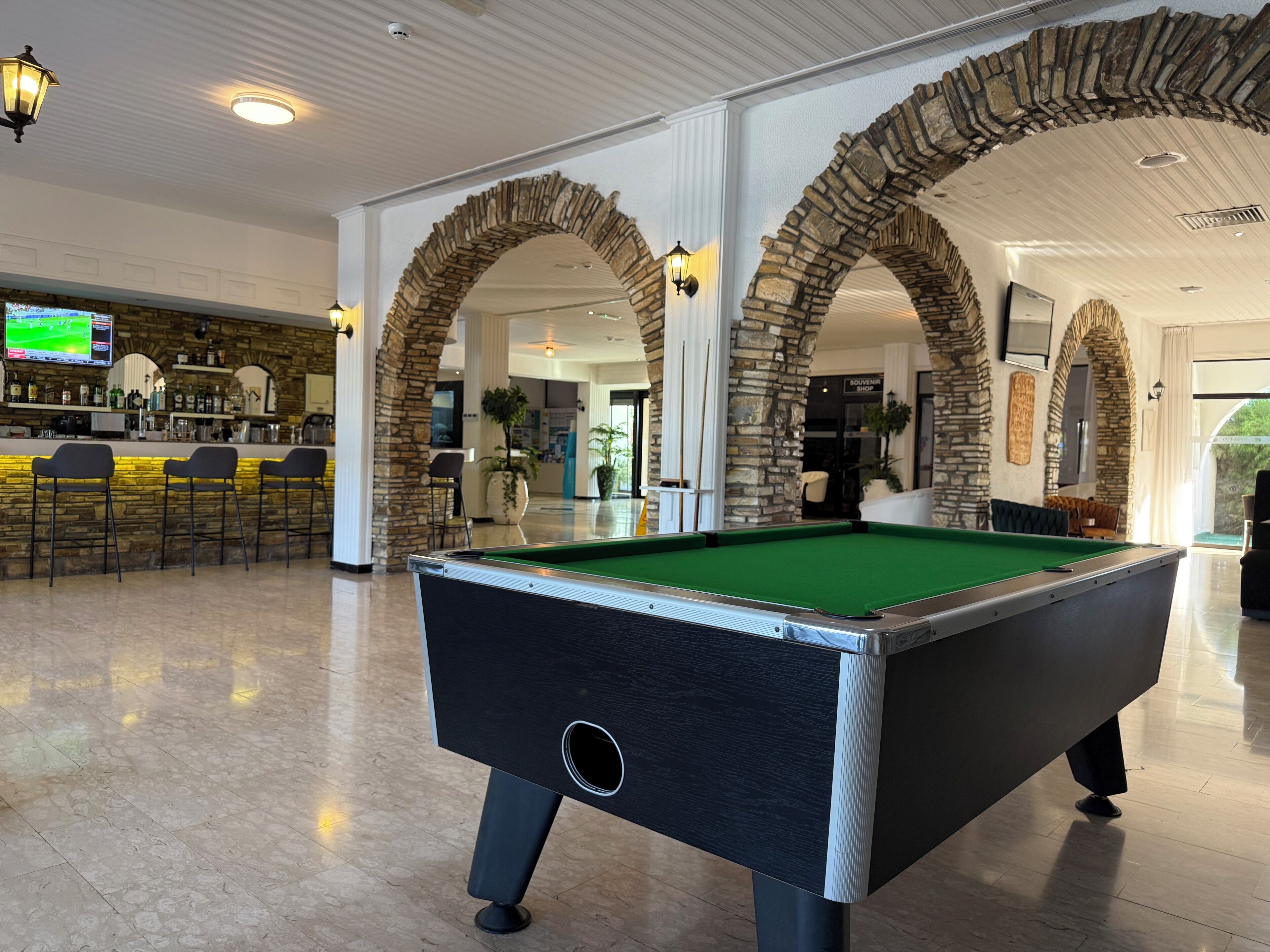 A pool table in a spacious room with stone arches and a bar area in the background.