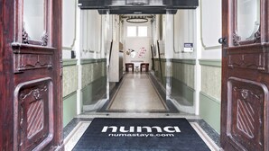 En hotelindgang med en sort dørmåtte med teksten "numastays.com" og et skilt med en besked.