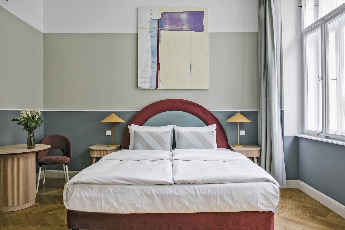 A hotel room with a large bed, two bedside tables, a chair, and a painting on the wall.