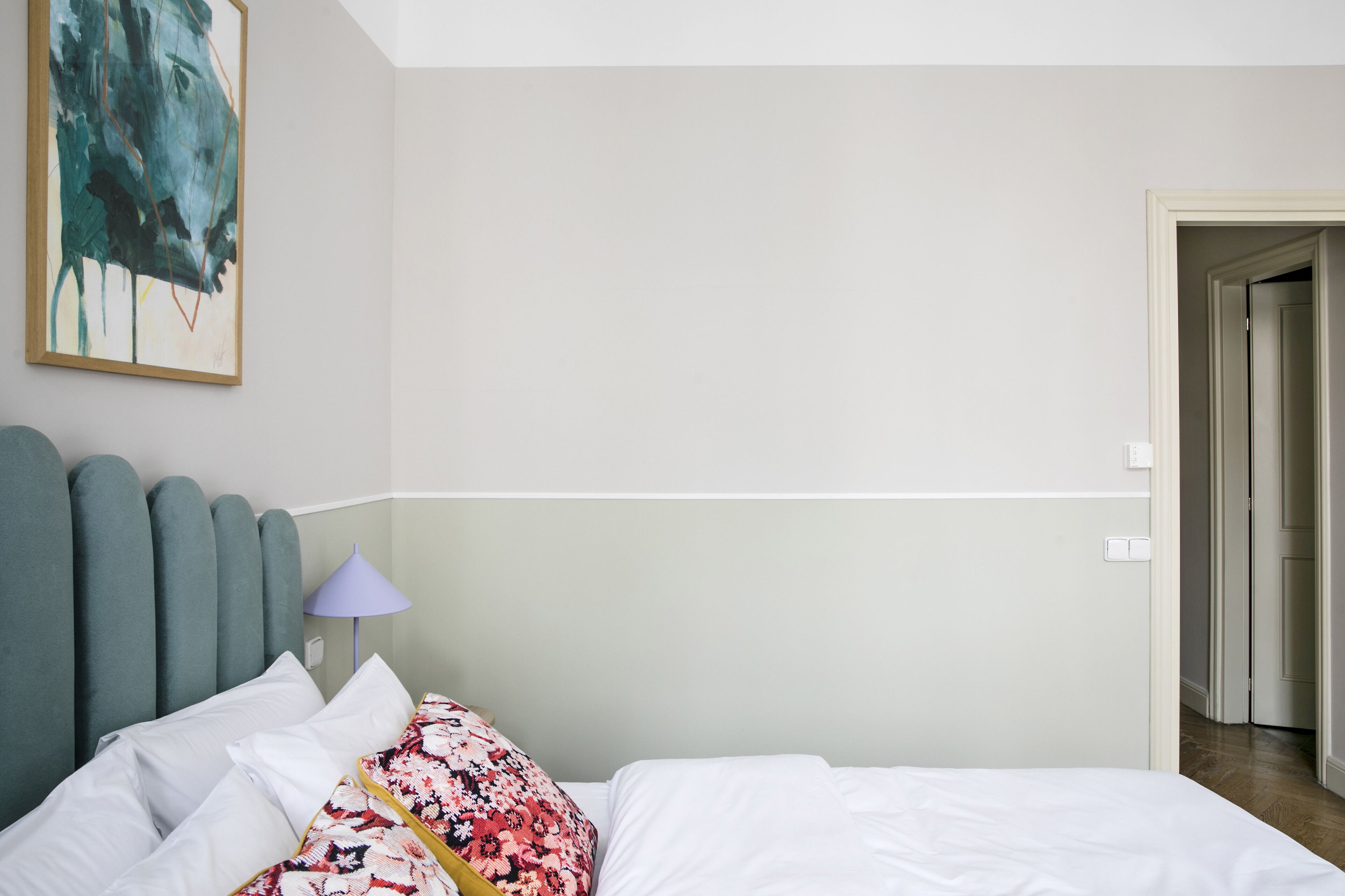 A hotel room with a bed, a headboard, a lamp, and a painting on the wall.