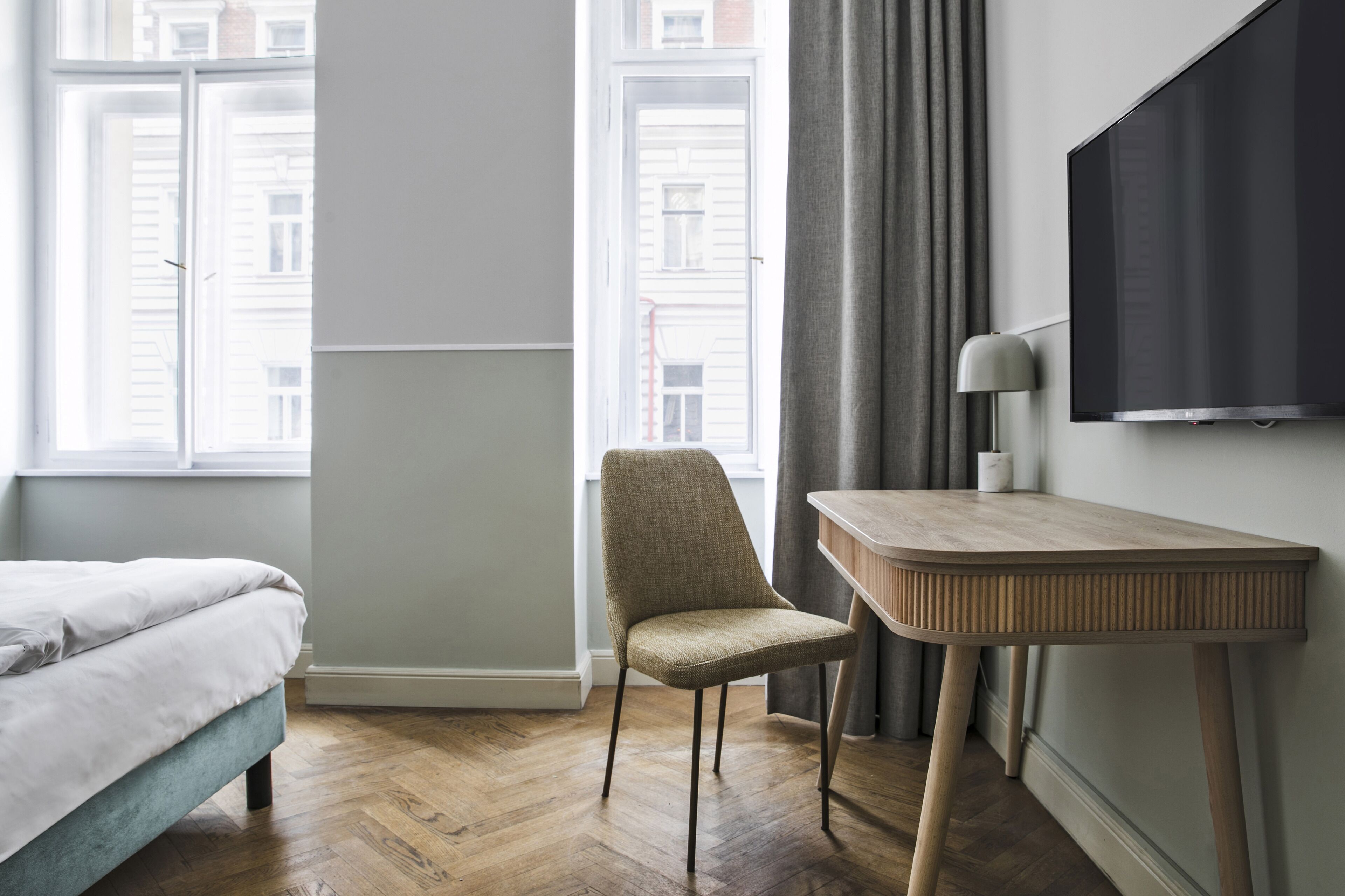 Habitación de hotel con cama, una silla, una mesita, televisor y ventana con cortinas.