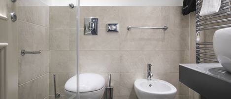 A modern bathroom with a toilet, bidet, and a glass shower enclosure.