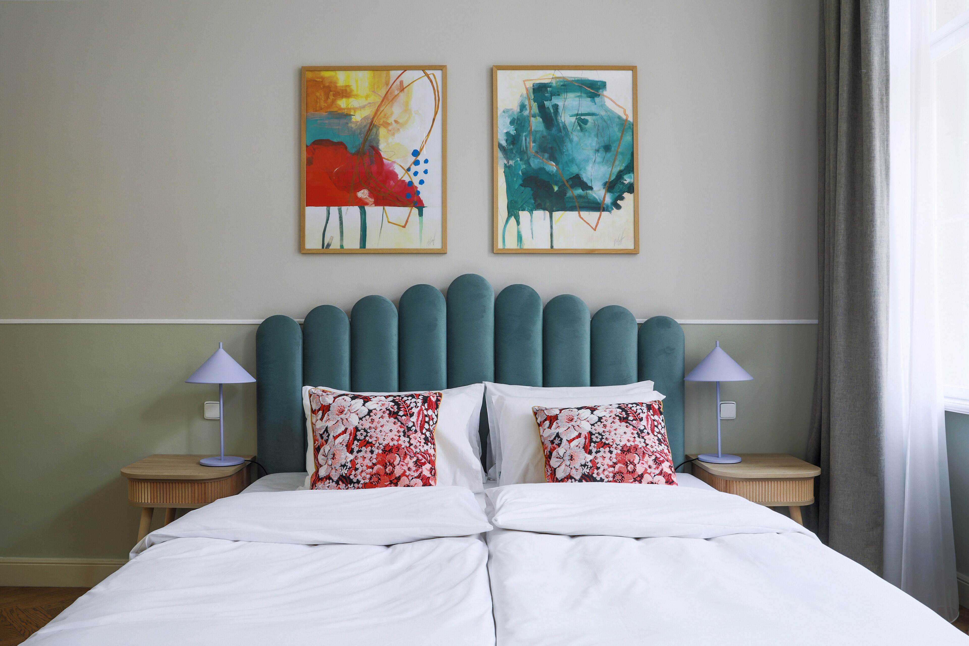 A neatly made bed with floral pillows, a teal headboard, and two wall-mounted paintings.