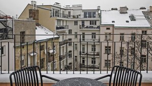 En balkon med to stole og et bord, der kigger ud over en række høje bygninger med egne balkoner og et sneklædt tag.