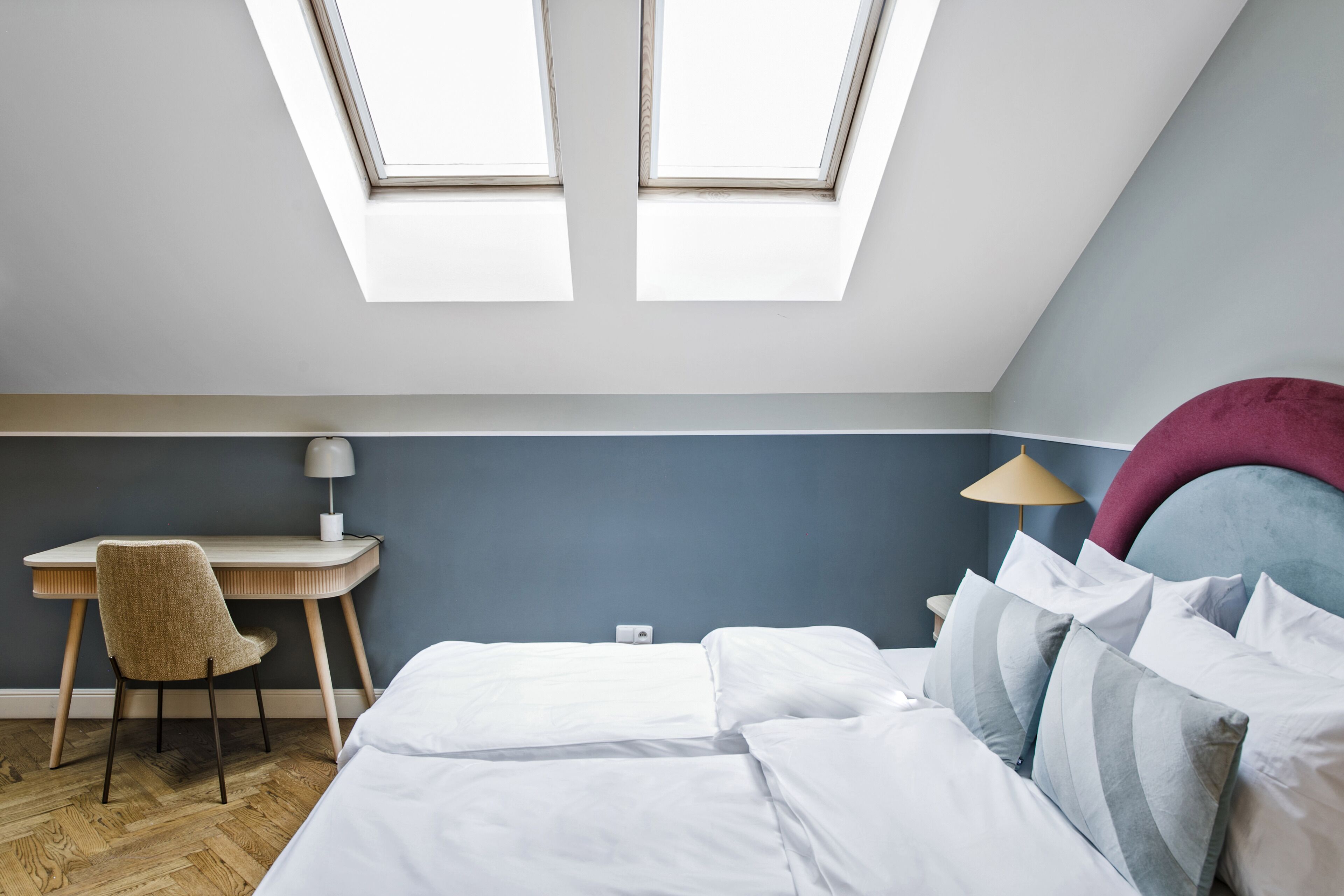 A bedroom with a bed, a desk, and two skylights.