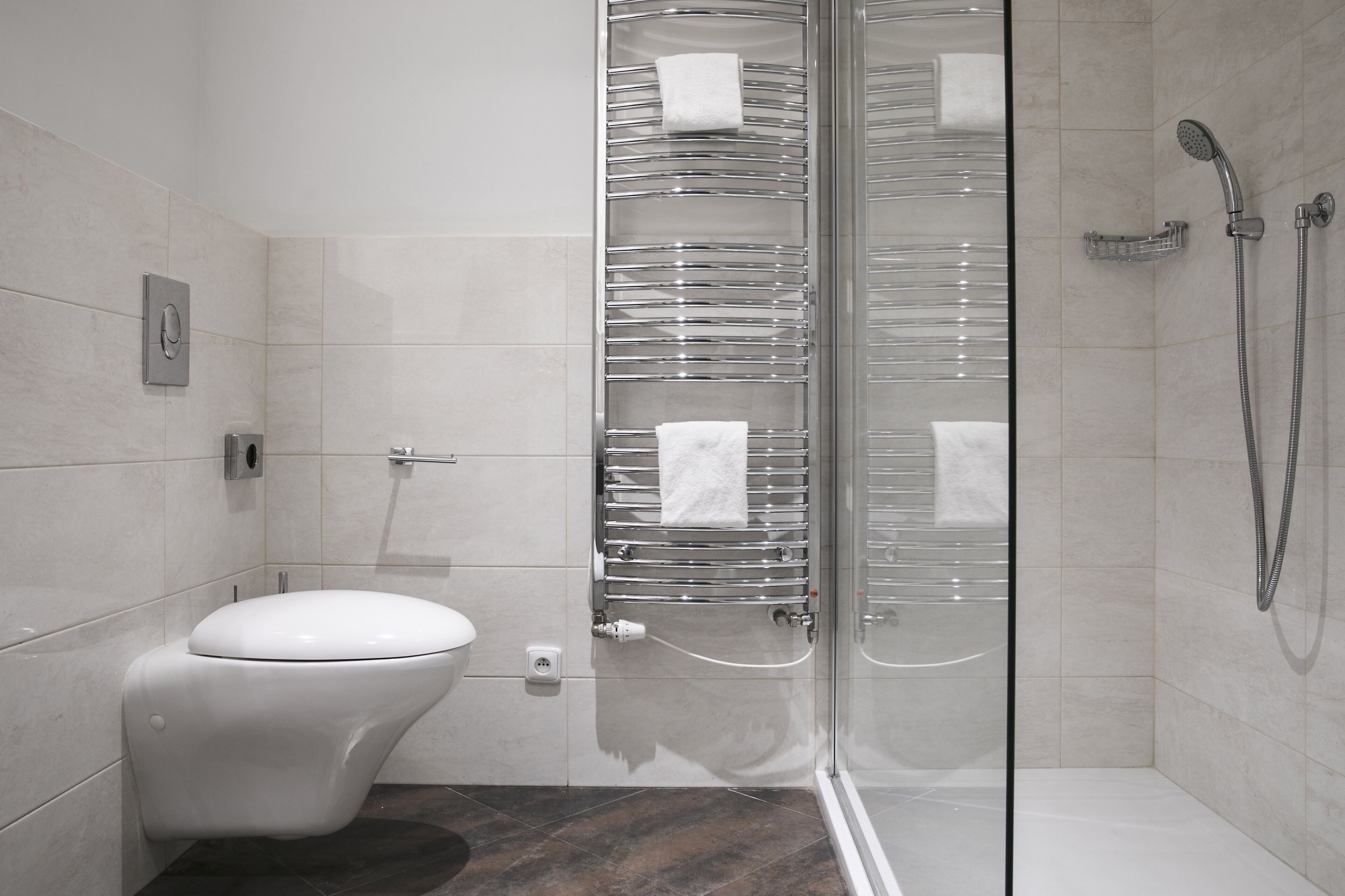 A modern bathroom with a glass shower enclosure, a white toilet, and a chrome towel rack.