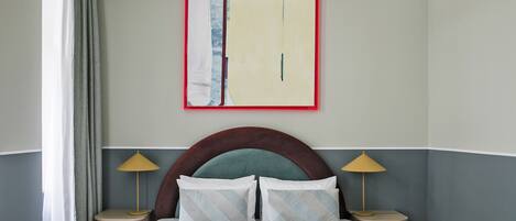 A neatly made bed with a headboard, two bedside tables with lamps, and a large abstract painting on the wall.