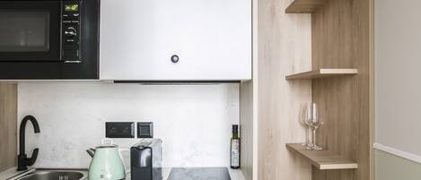 A modern kitchen with a microwave, kettle, toaster, and a wine bottle on the counter.