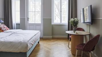 A bedroom with a bed, a round table with a chair, and a TV mounted on the wall.