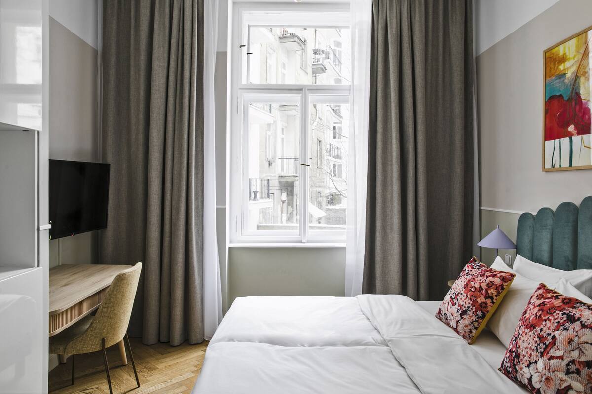 A hotel room with a bed, a desk, and a window with curtains.