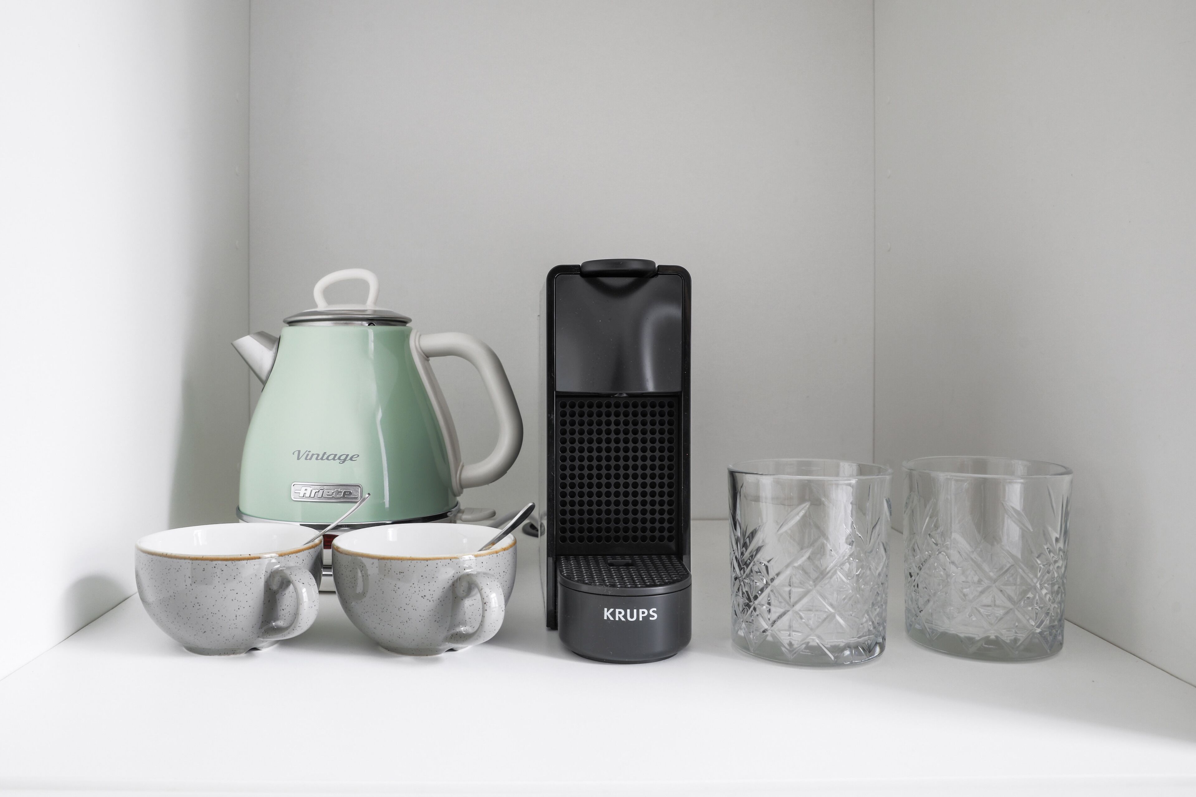 A kitchen setup with a vintage-style electric kettle, a Krups coffee maker, two cups, and two glasses.