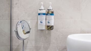 Un baño con un espejo redondo, dos botellas de crema corporal REN y un lavamanos blanco.