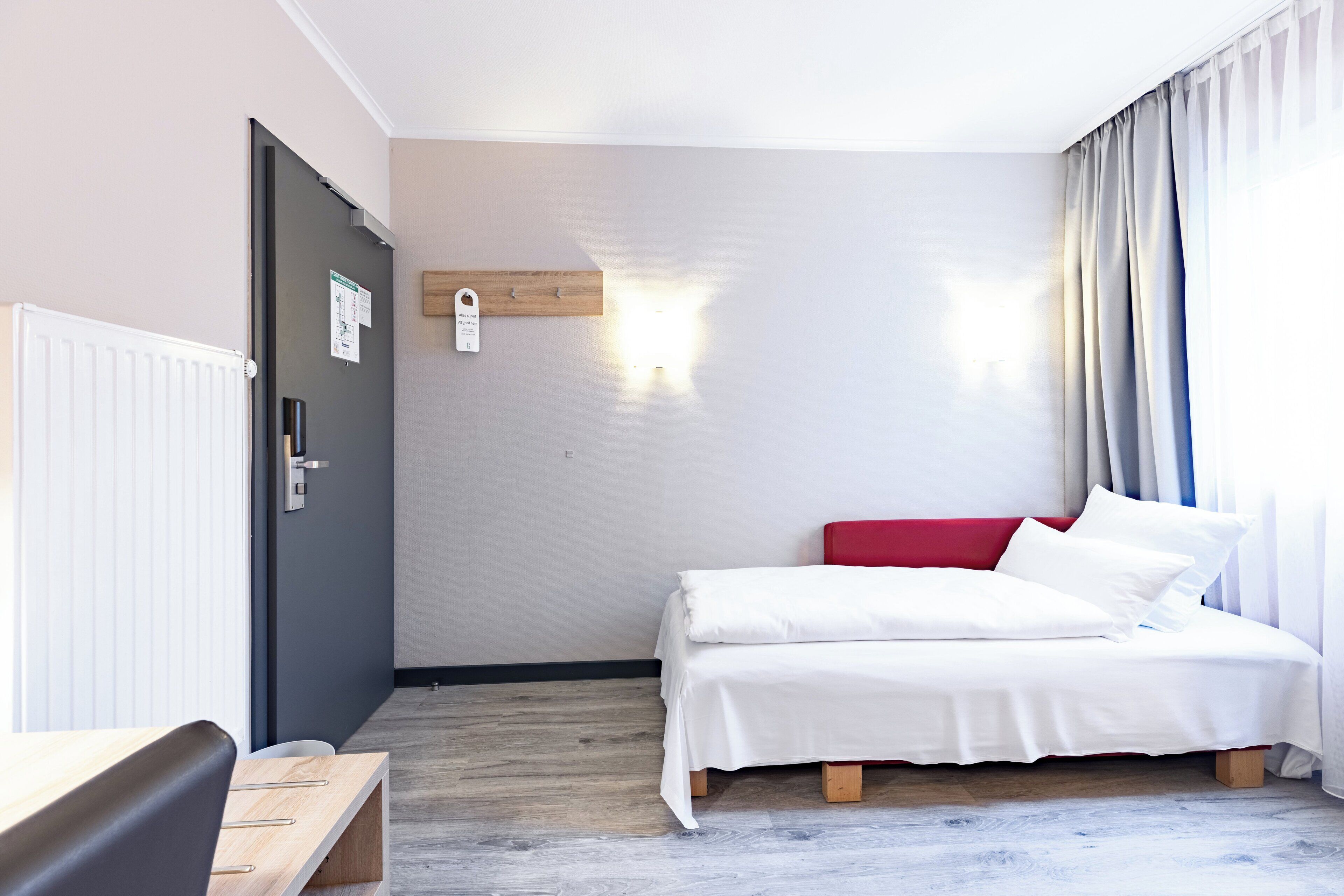 A hotel room with a bed, a desk, and a window with curtains.
