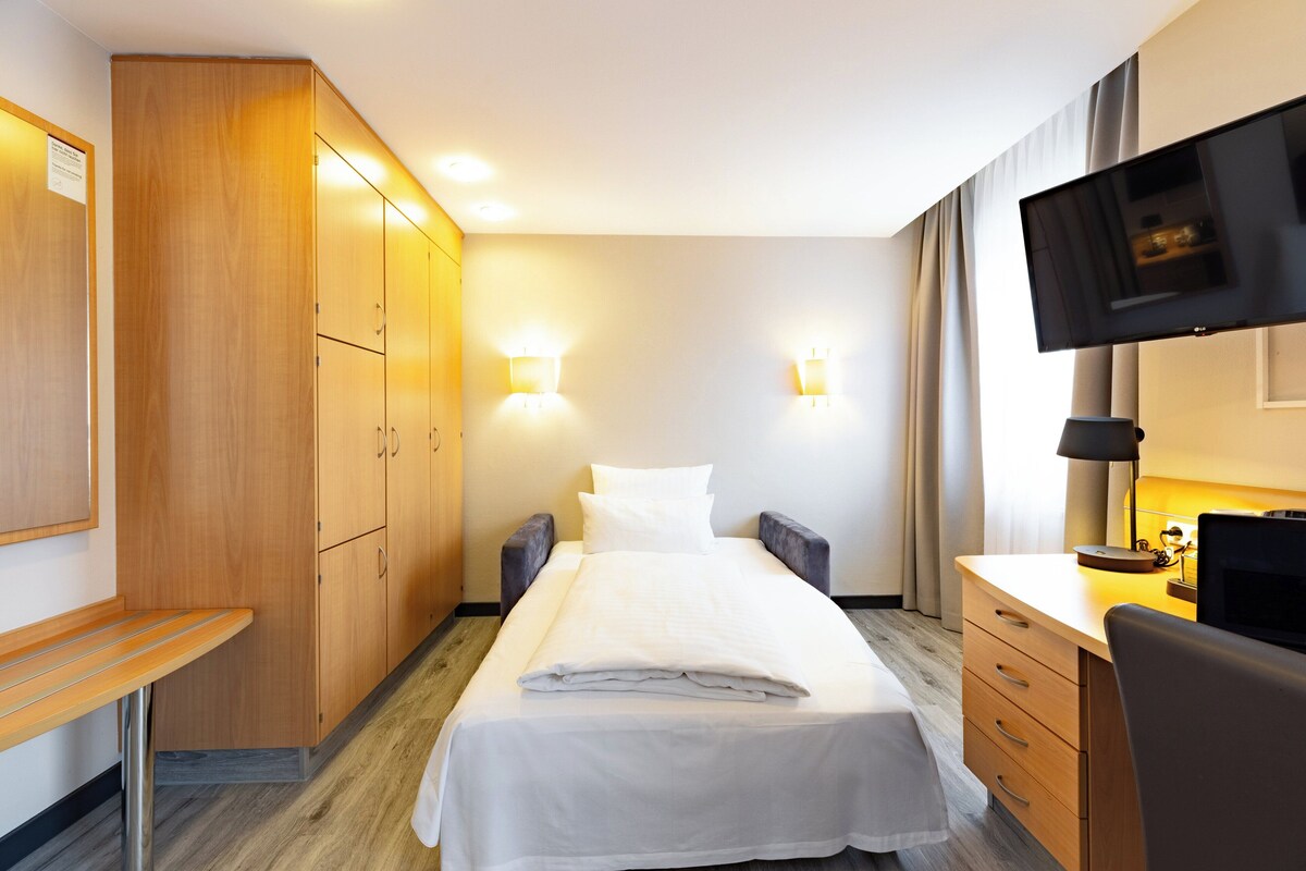 Una habitación de hotel con una cama, un escritorio, un televisor y un armario.