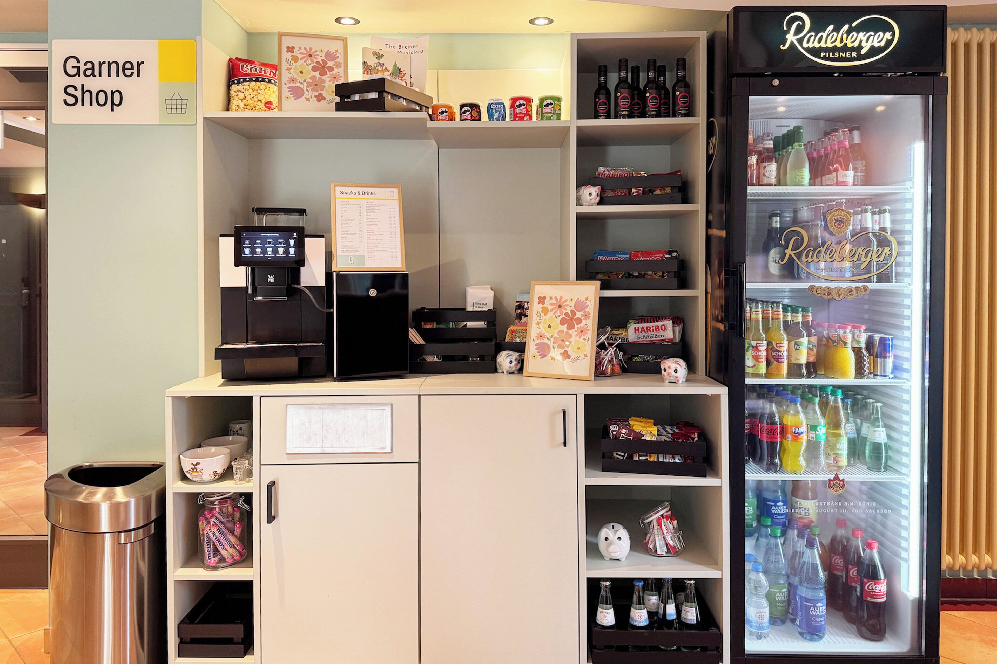 A snack bar with a coffee machine, a refrigerated display of beverages, and a trash bin.
