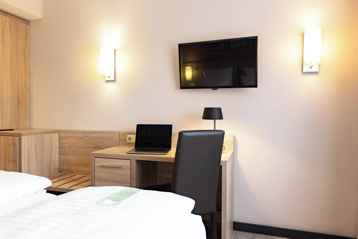 Habitación de hotel con cama, escritorio, laptop, silla y televisor montado en la pared.