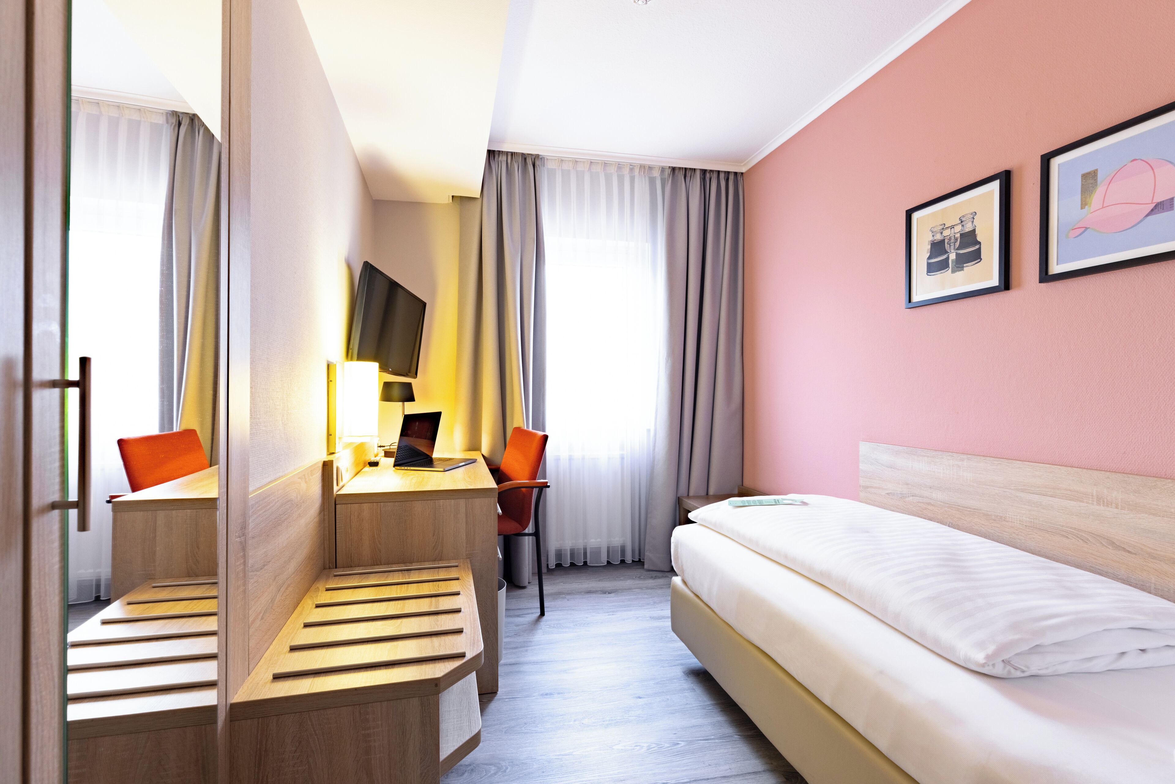 Una habitación de hotel con cama, escritorio con silla, televisión y ventana con cortinas.