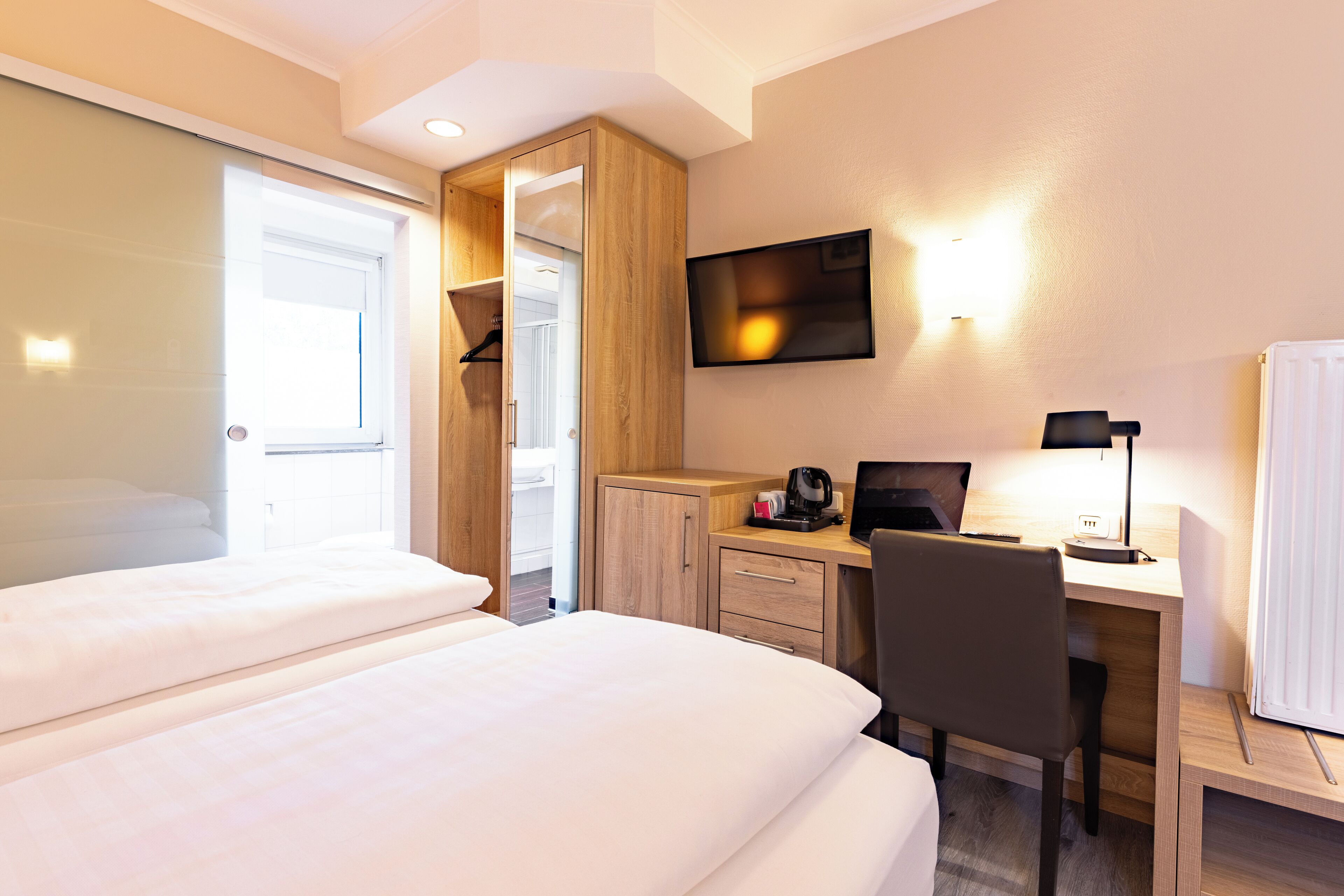 A hotel room with two beds, a desk with a computer, a chair, a TV, and a wardrobe.