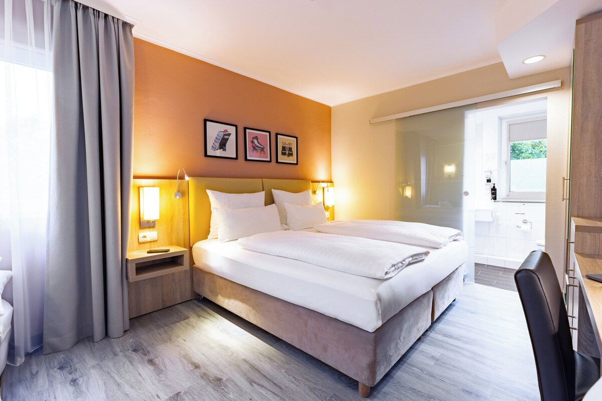 Una habitación de hotel con una cama grande, mesitas de noche con lámparas, un escritorio y una silla.