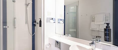 Un baño moderno con ducha envuelta en vidrio, un espejo grande y un lavabo blanco.