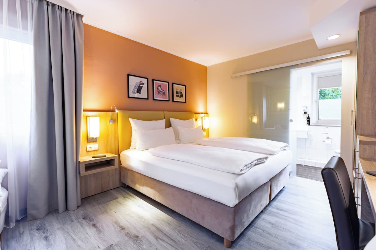 Una habitación de hotel con una cama grande, mesitas de noche con lámparas, un escritorio y una silla.