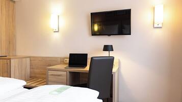 A hotel room with a bed, a desk with a laptop, a chair, and a TV mounted on the wall.