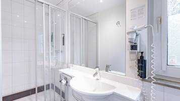 Un baño moderno con cabina de ducha de vidrio, lavamanos blanco y espejo.