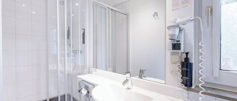 Un baño moderno con cabina de ducha de vidrio, lavamanos blanco y espejo.