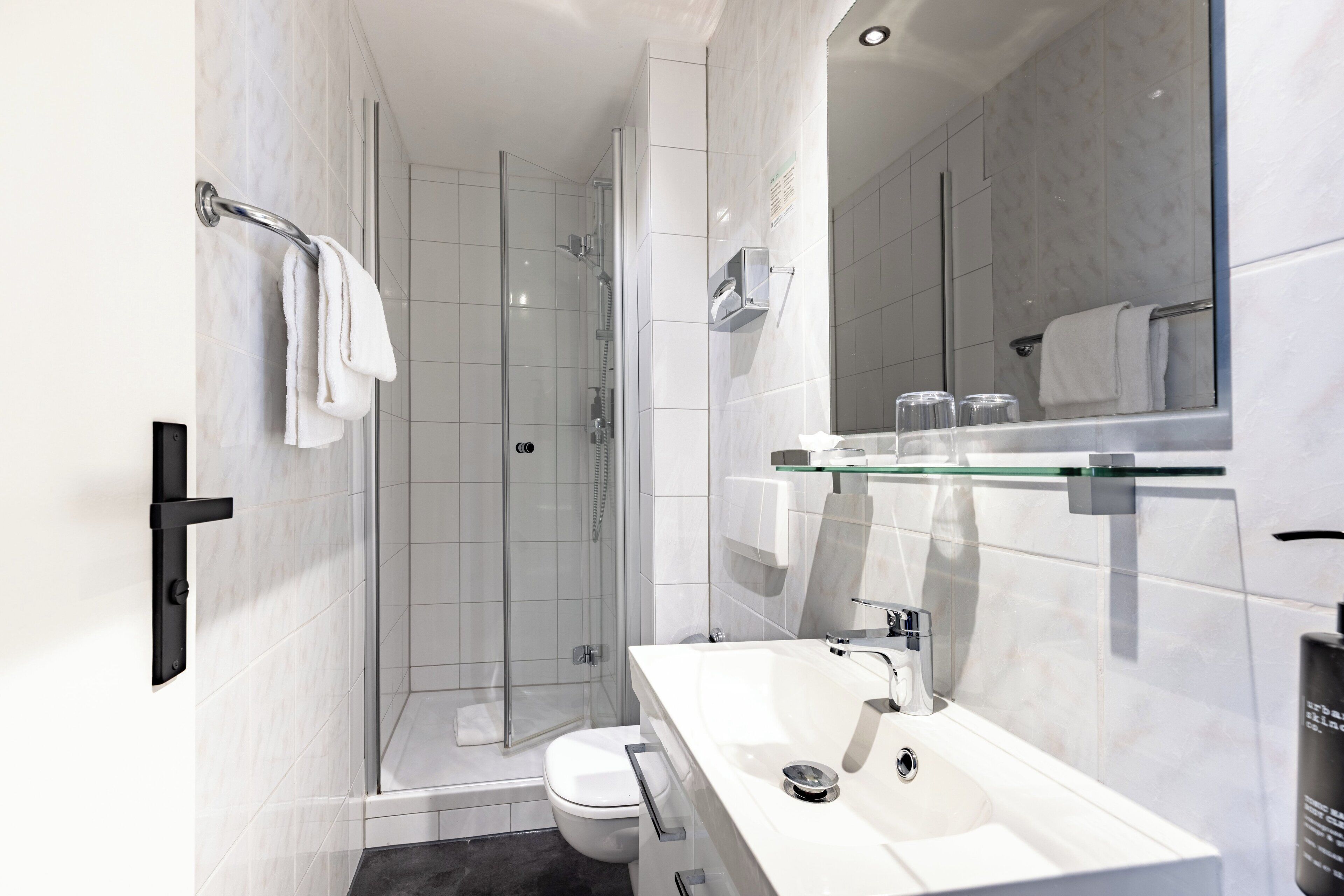 A modern bathroom with a glass shower enclosure, a white sink with a mirror above, and a toilet.