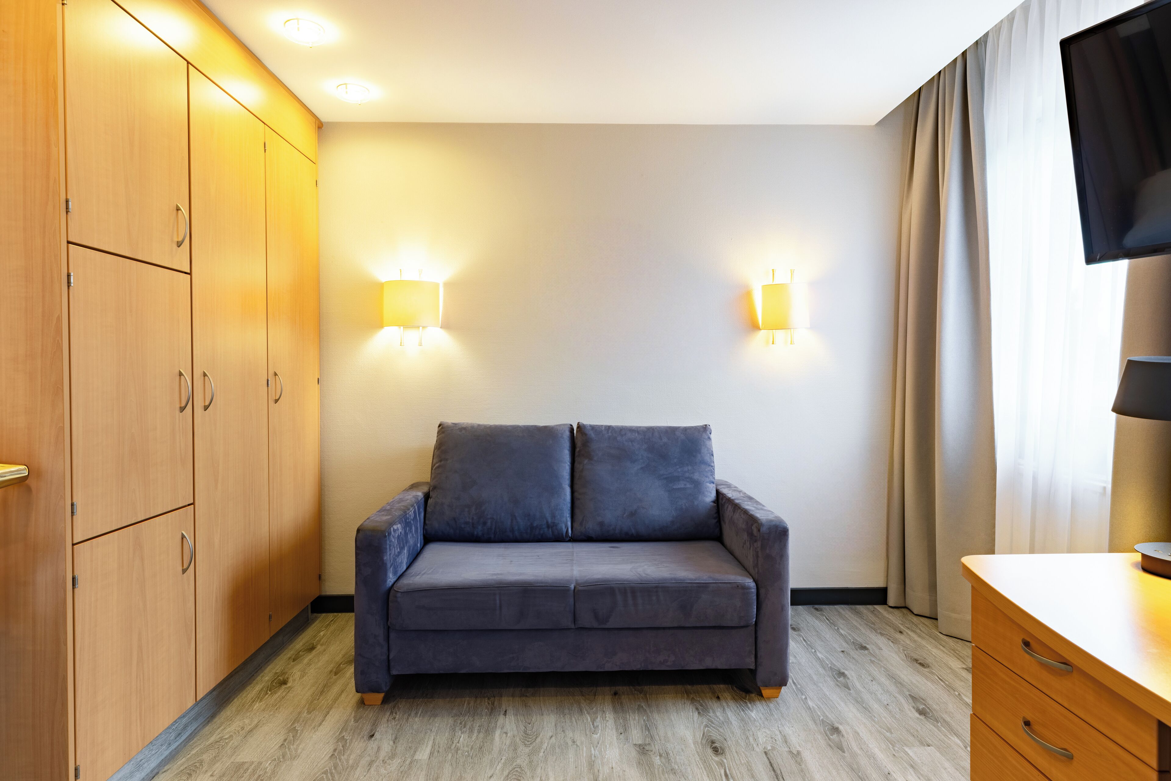 Una habitación con sofá gris, armario de madera y televisor en la pared.