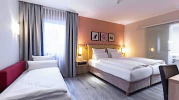Ein Hotelzimmer mit zwei Betten, einem roten Kopfteil, Holzboden und einem großen Fenster mit Vorhängen.