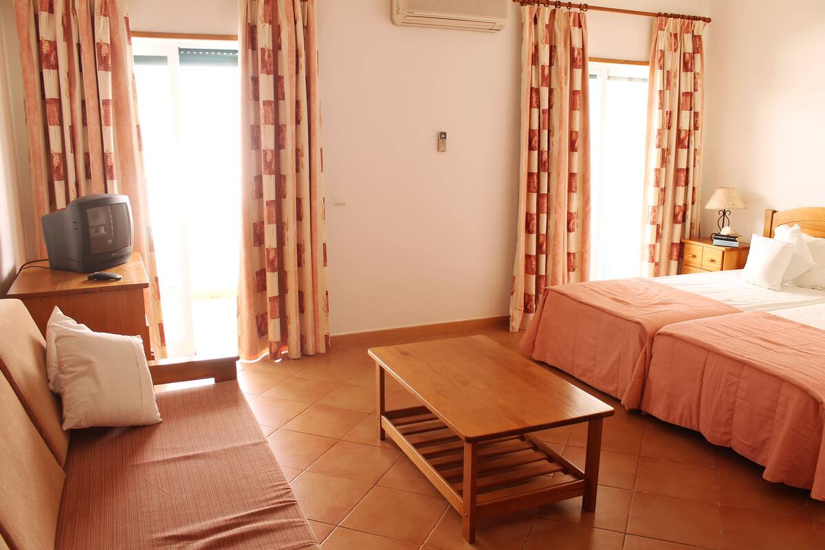 Una habitación con dos camas, una mesa de madera, un televisor y cortinas.
