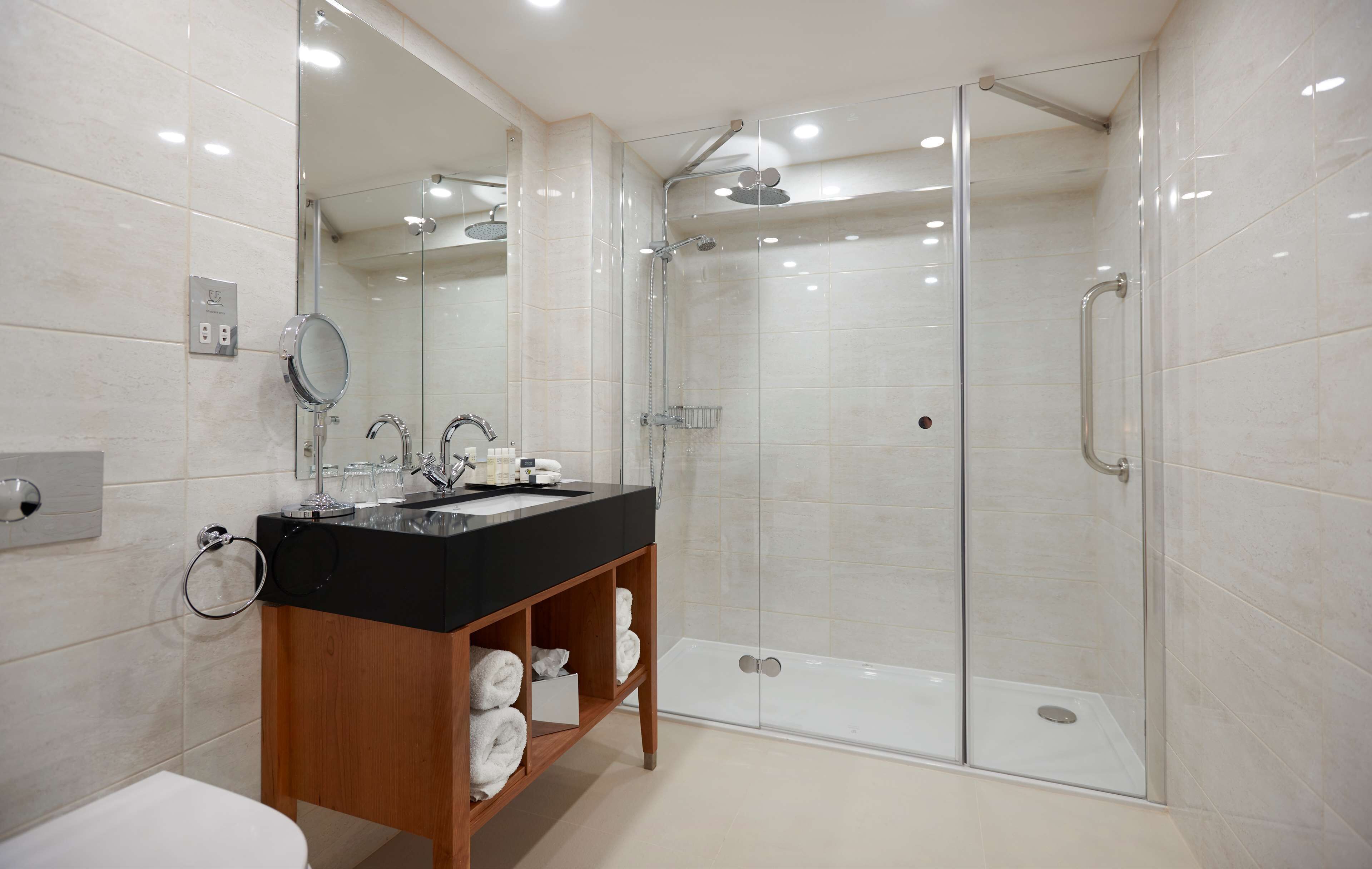 A modern bathroom with a glass-enclosed shower, a black sink vanity, and a mirror.