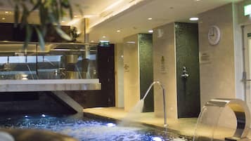 Un área de piscina interior moderna con una fuente de agua, un reloj y un cartel que indica un espacio de spa o relajación.