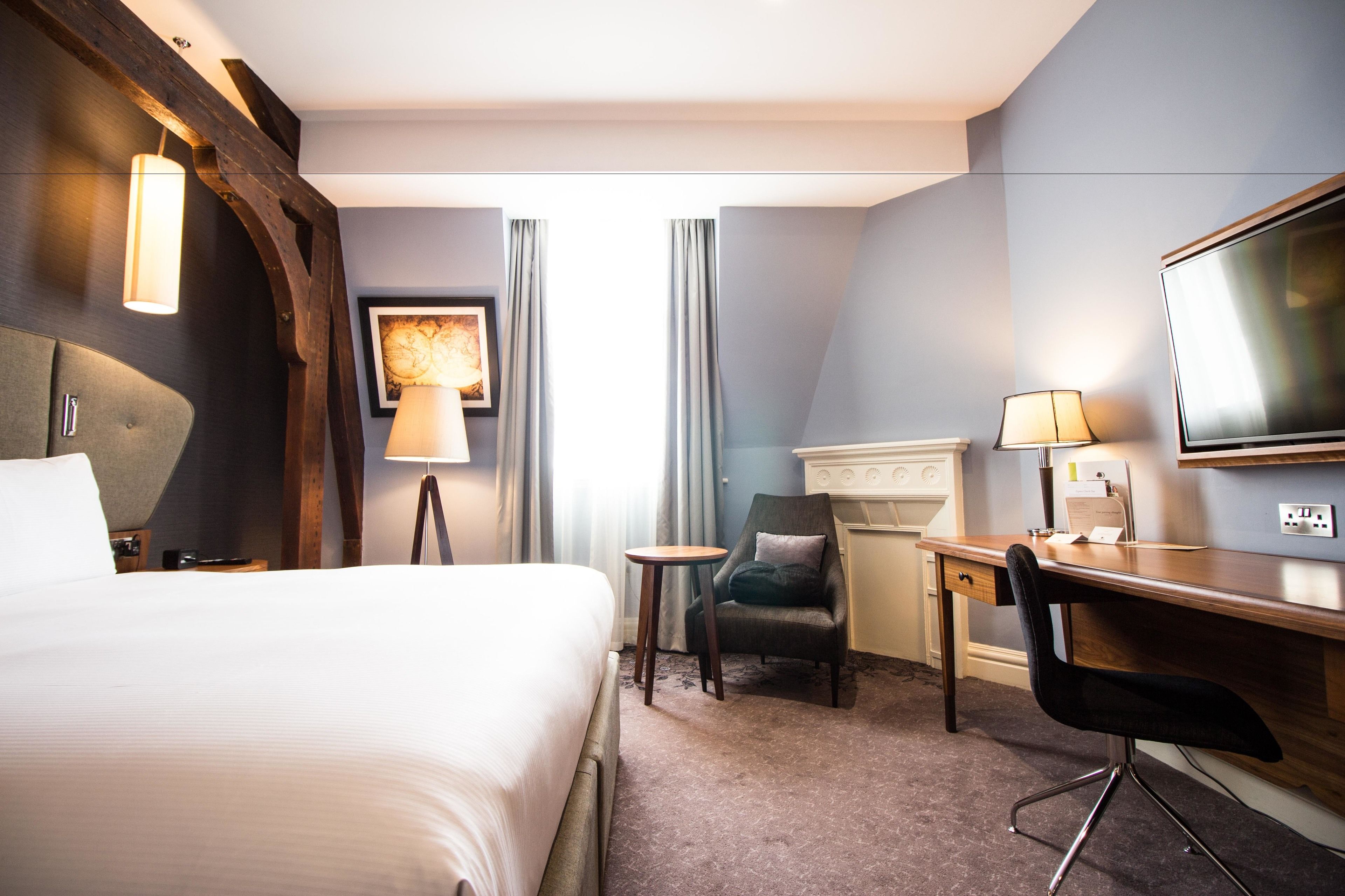 Ein Hotelzimmer mit einem großen Bett, einem Schreibtisch, einem Sessel, einem Fernseher und einer Lampe.