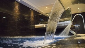 A modern indoor pool with a waterfall feature, surrounded by dark tiled walls and a glass railing. - DoubleTree By Hilton Hotel & Spa Liverpool (Liverpool)
