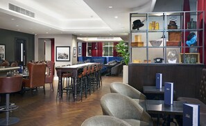 A modern hotel lobby with a long dining table, multiple seating options, and a decorative glass display case. - DoubleTree By Hilton Hotel & Spa Liverpool (Liverpool)