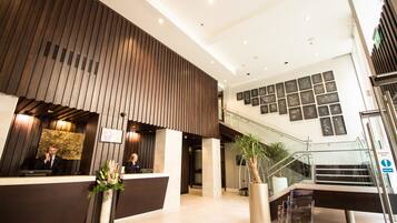A modern hotel lobby with a reception desk, a staircase, and a wall with framed pictures.