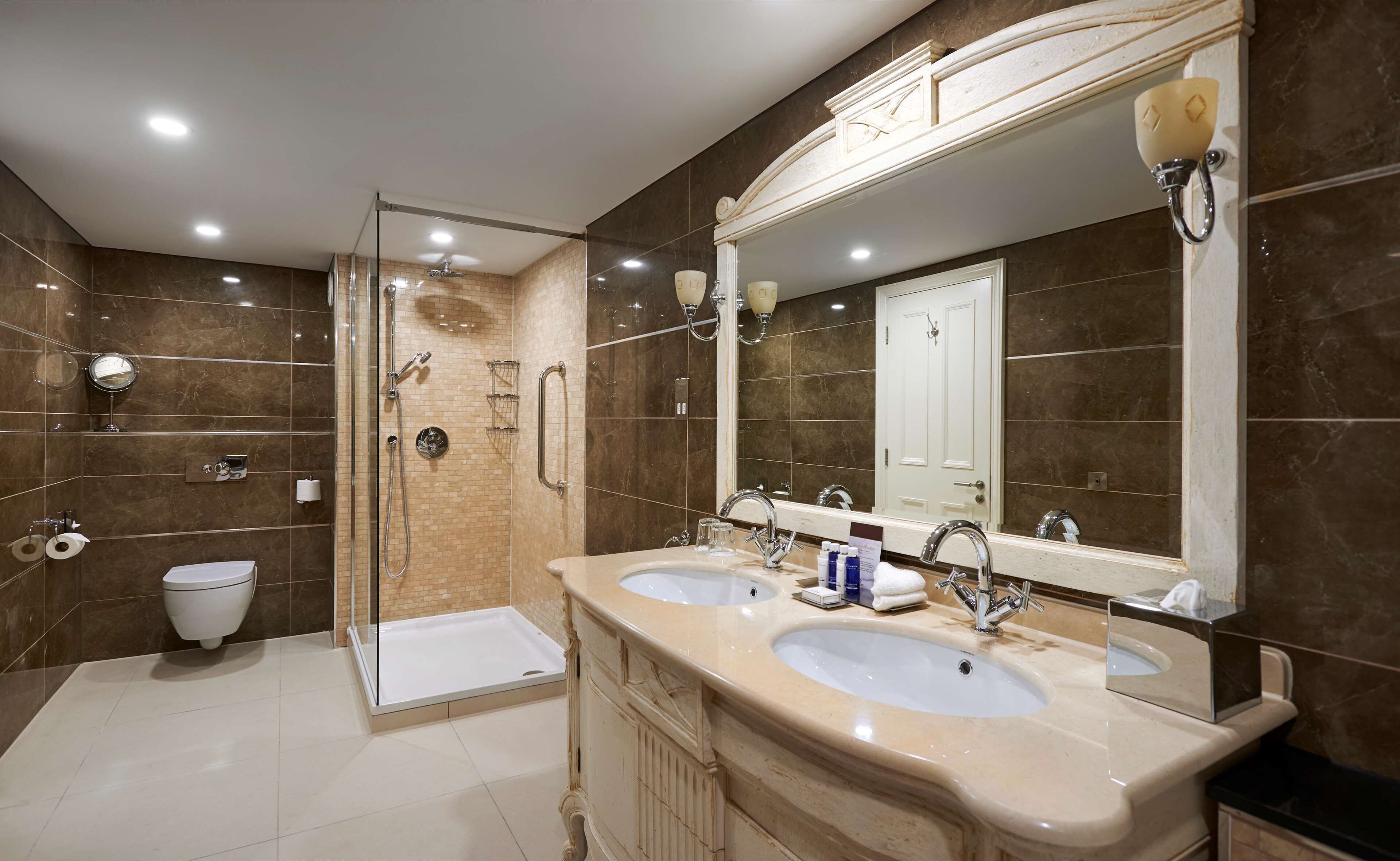 A modern bathroom with two sinks, a glass shower enclosure, a toilet, and a large mirror.