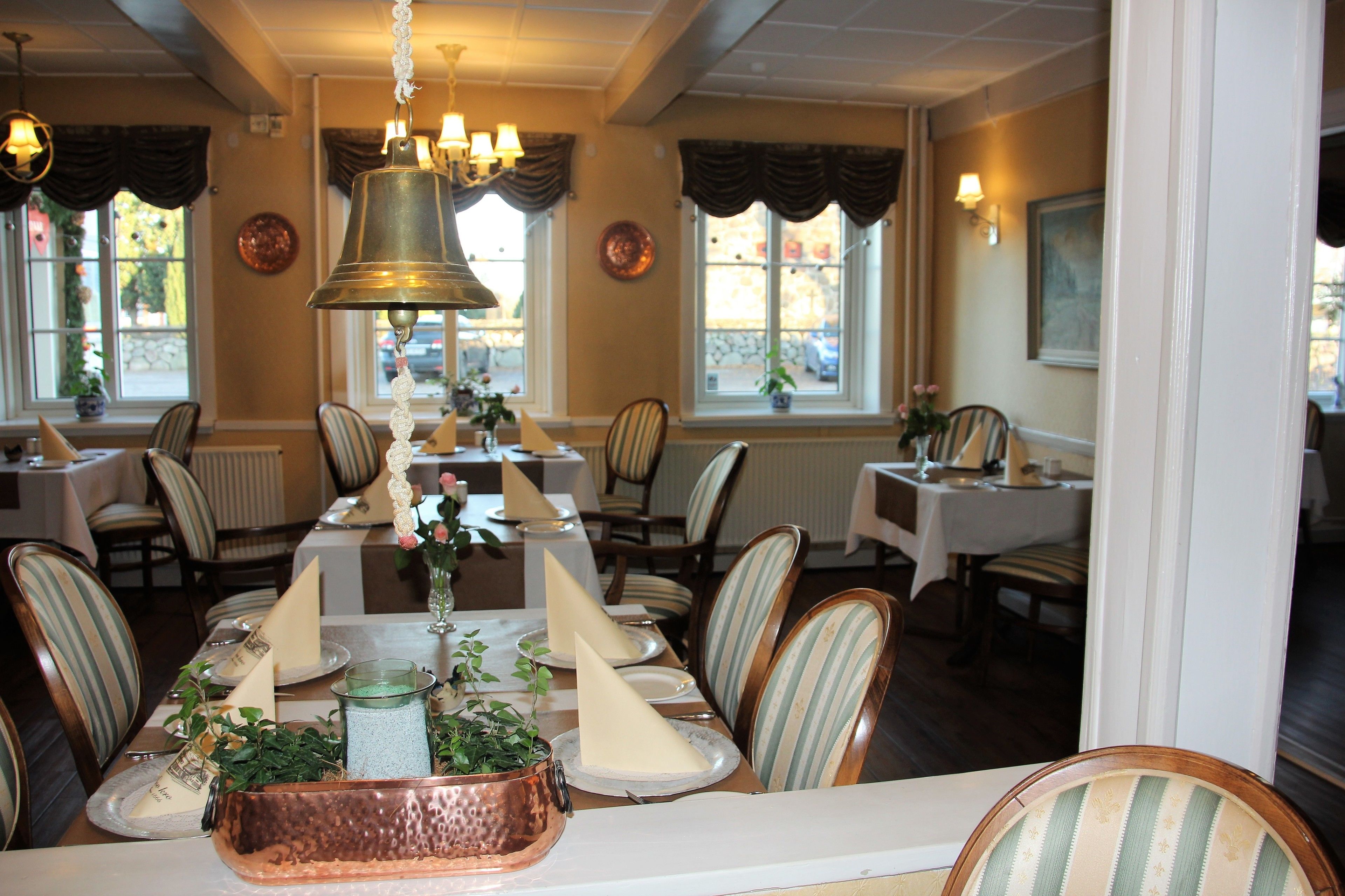 A dining area with striped chairs, a long table with a copper serving tray, and a hanging bell.
