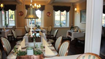 A dining area with striped chairs, a long table with a copper serving tray, and a hanging bell.